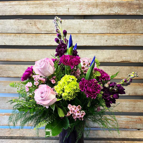 Mixed bouquet of pink roses, purple blooms, and green hydrangea in a purple vase