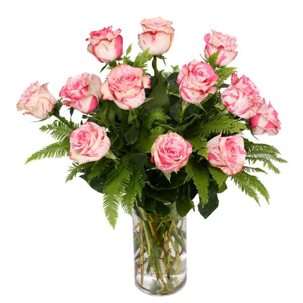 Pink and white roses in a clear glass vase with fern foliage