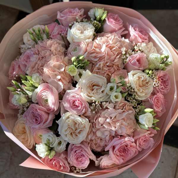 Pink and white bouquet of roses, hydrangeas, and ranunculus wrapped in pink paper