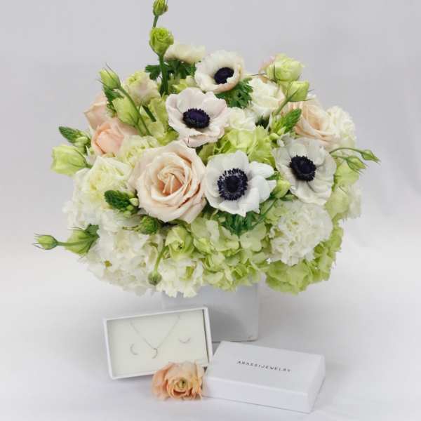 Bouquet of pale roses and white anemones in a clear vase with jewelry boxes below