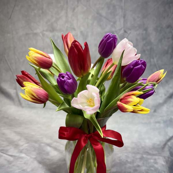 Bouquet of multicolored tulips in a glass vase with a red ribbon