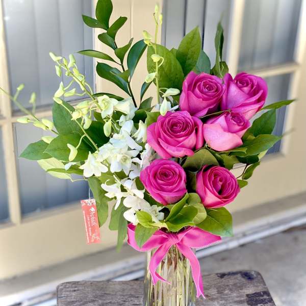 Pink roses and white orchids in a glass vase with a pink ribbon