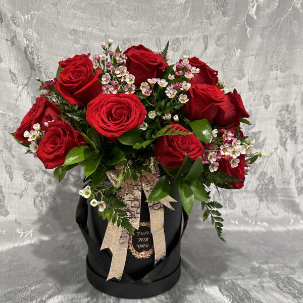 Red roses arranged in a black hatbox with pink filler flowers.