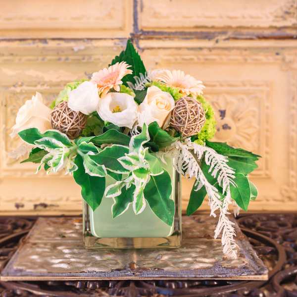 Floral arrangement in a square glass vase with white and peach blooms