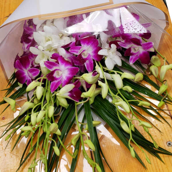 Wrapped bouquet of purple and white orchids with long green blades and a purple bow
