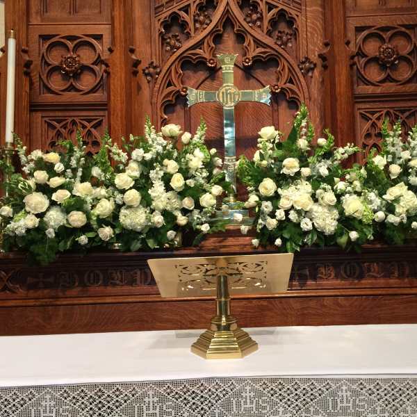 White floral arrangements flank a church altar with a cross.