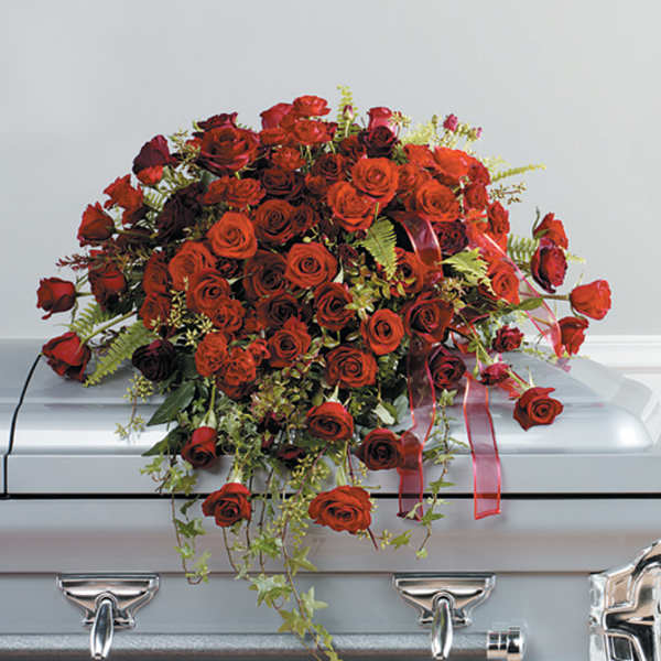 Red rose casket spray with trailing greenery and ribbon