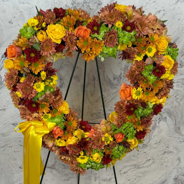 Heart-shaped floral wreath on a stand with a yellow ribbon