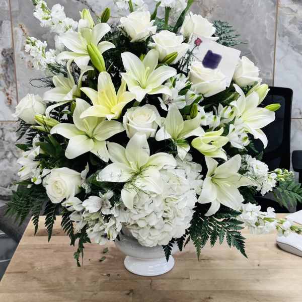 White lilies and roses arranged in a white pedestal vase