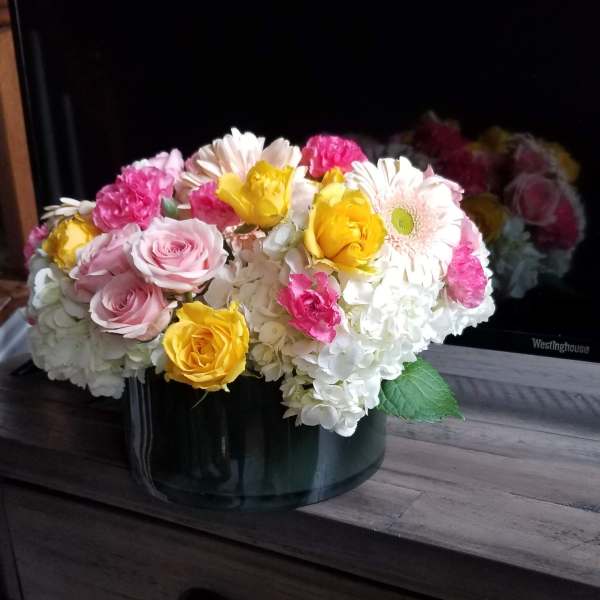 Mixed pink, yellow, and white flowers arranged in a dark vase