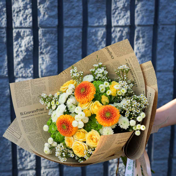 Bouquet of yellow roses and orange gerbera daisies wrapped in newspaper-style paper