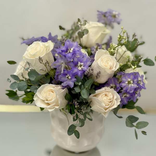 White roses and purple flowers arranged in a white vase