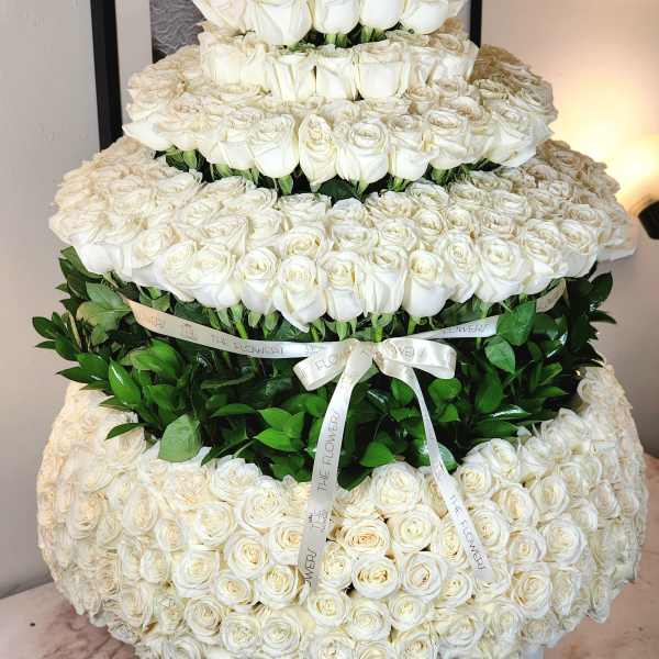 Tiered arrangement of white roses with green foliage and a ribbon