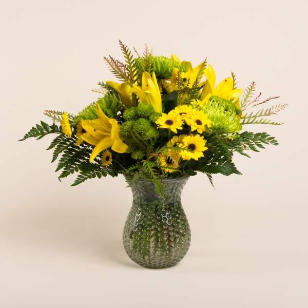 Yellow lilies and daisies in a textured glass vase