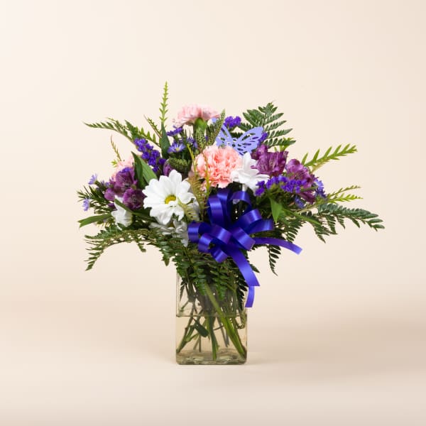 Mixed bouquet of pink, purple, and white flowers in a glass vase with a purple ribbon