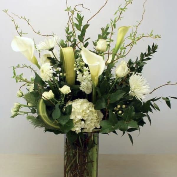 White calla lilies and chrysanthemums in a tall glass vase
