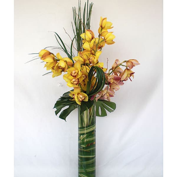 Tall arrangement of yellow and pink orchids in a green glass vase