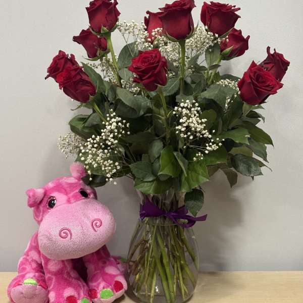 Red roses in a glass vase beside a pink plush hippo