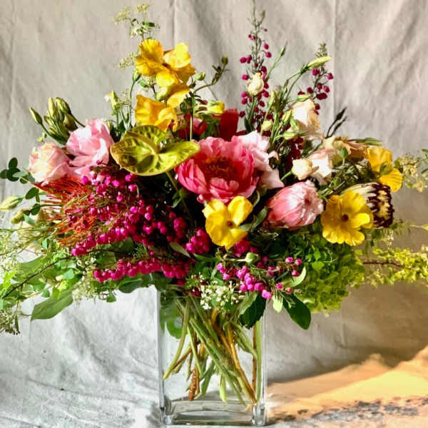 Mixed bouquet of pink, yellow, and white flowers in a clear glass vase