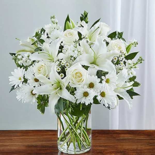 White lilies, roses, and daisies arranged in a clear glass vase