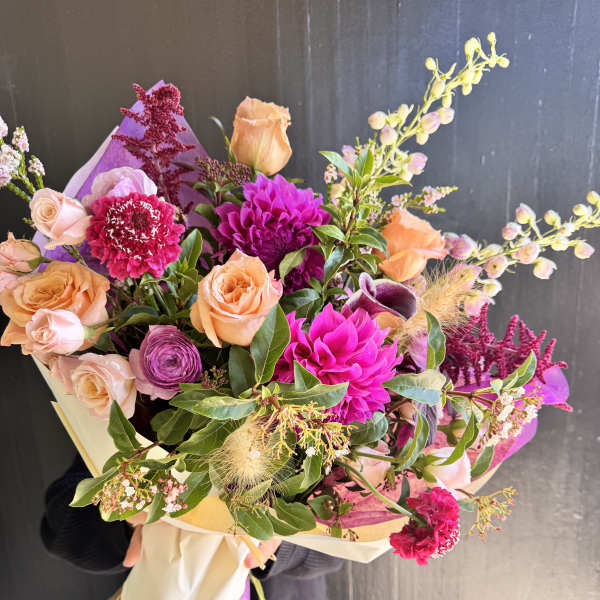 Hand-tied bouquet of peach and magenta flowers wrapped in paper
