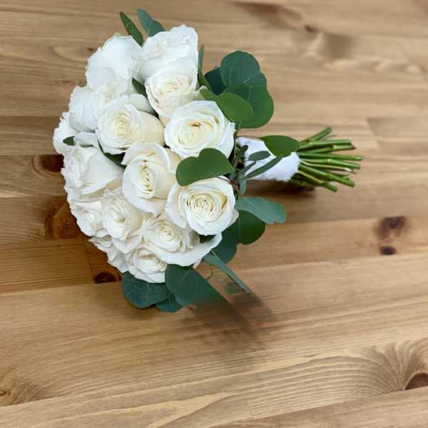 White rose bouquet with green foliage on a wooden surface
