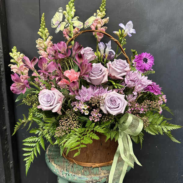 Basket arrangement of lavender roses and pink flowers with butterflies