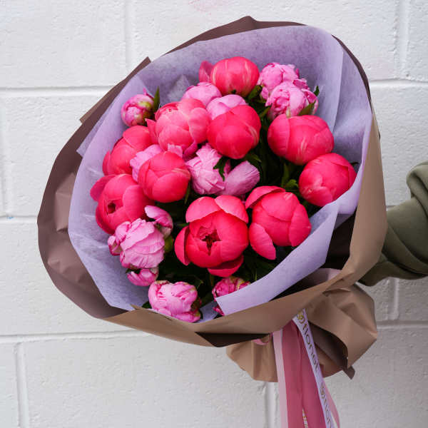 Bouquet of bright pink peonies wrapped in brown and lavender paper