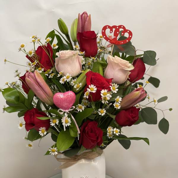 Bouquet of red roses, pink lilies, and daisies in a white vase