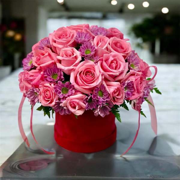 Pink roses and purple daisies in a red hatbox with ribbon