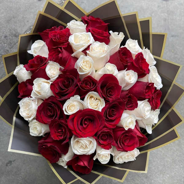 Round bouquet of red and white roses wrapped in layered dark paper with gold-edged points