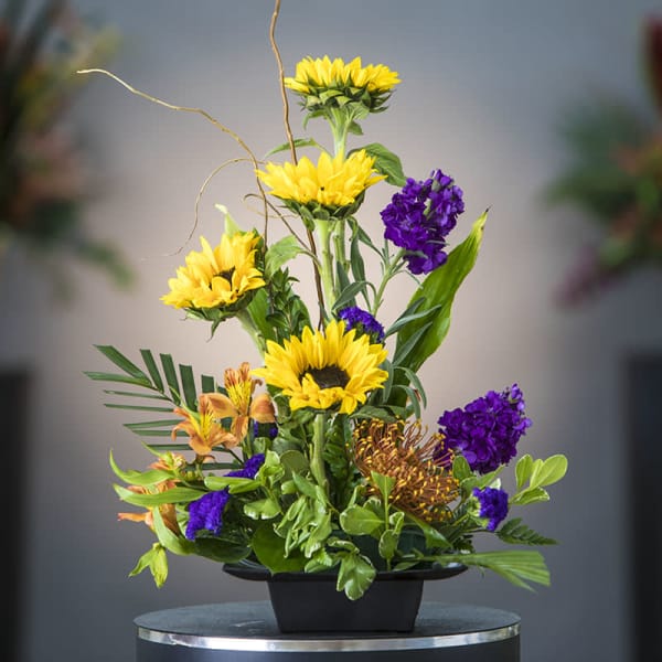 Tall floral arrangement with yellow sunflowers and purple blooms in a black container