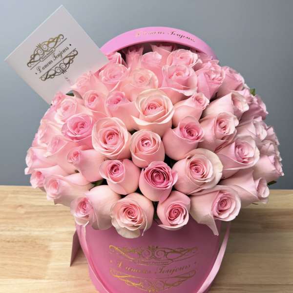 Pink roses arranged in a round pink hat box with a card attached