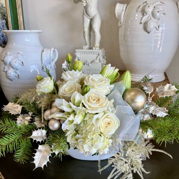 White roses and lilies arranged with holiday ornaments and ribbon