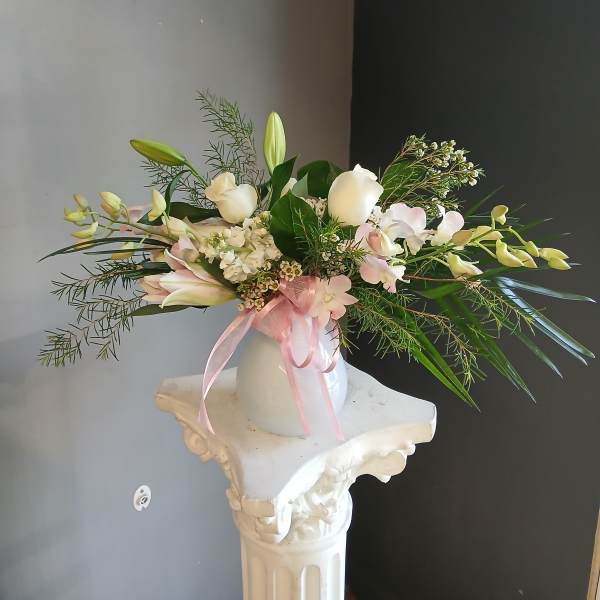 White floral arrangement with pink ribbon in a white vase