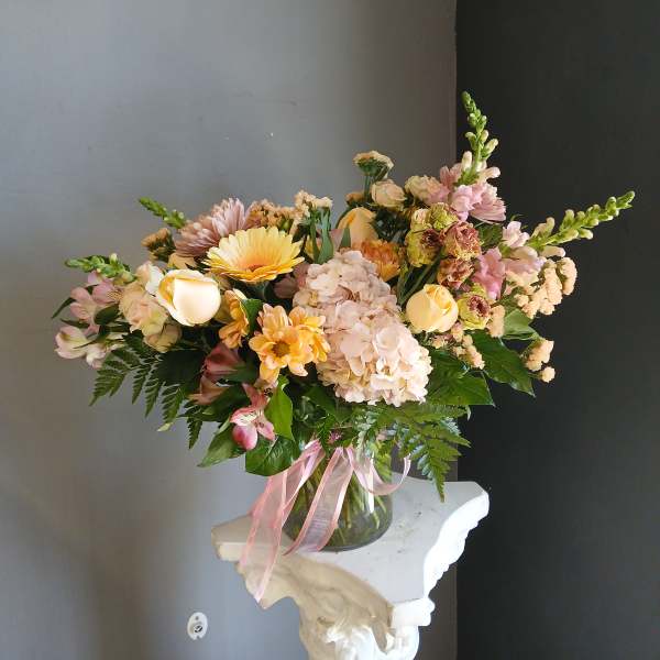 Pastel mixed flower arrangement in a glass vase with pink ribbon