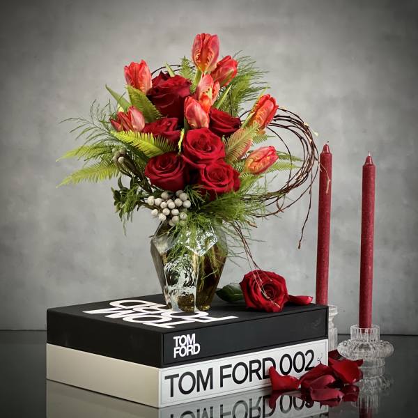 Red roses and tulips in a faceted glass vase with candles nearby