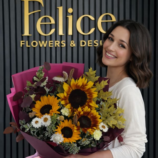 Woman holding a bouquet of sunflowers and small white flowers in pink wrap