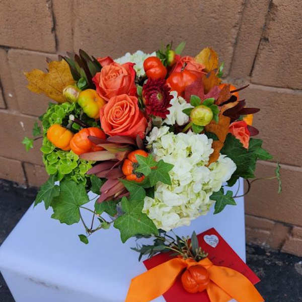 Hand-tied bouquet of orange roses and white hydrangeas with mini pumpkin accents and ivy, tied with an orange ribbon.
