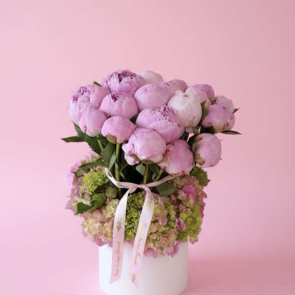 Pink peonies arranged in a white round box with a ribbon