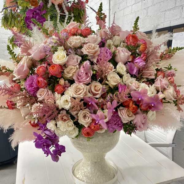 Large mixed bouquet of pink, cream, and purple flowers in a white vase