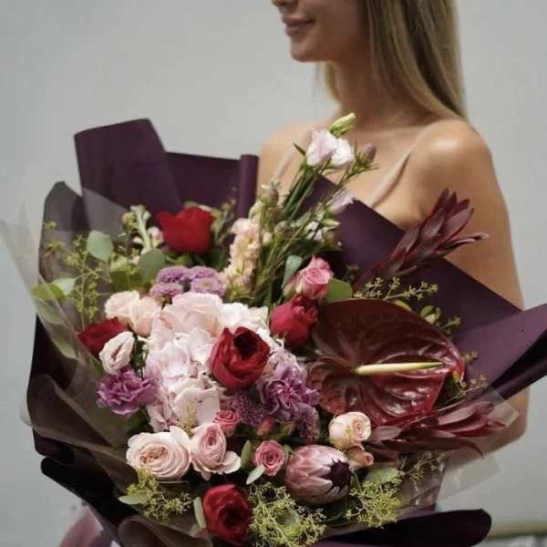 Large bouquet of pink and red flowers wrapped in dark paper