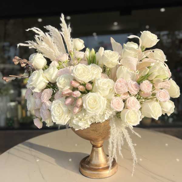 Cream and blush rose arrangement in a gold pedestal vase