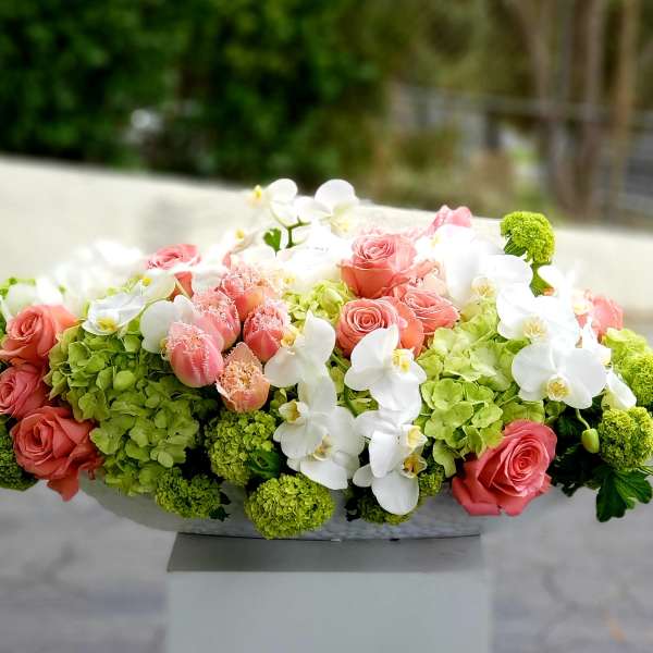 Pink roses and white orchids arranged with green hydrangeas in a low container