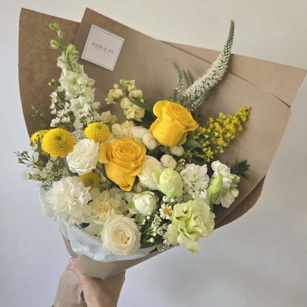 Hand-tied bouquet of yellow and white flowers wrapped in brown paper