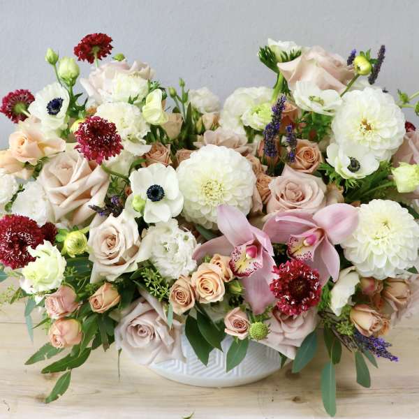 Mixed bouquet of blush roses, white blooms, and pink orchids in a white bowl vase