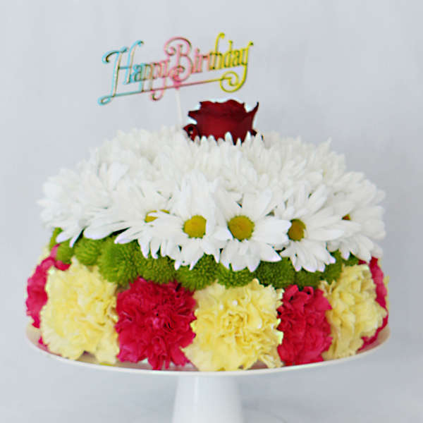 Colorful birthday cake topped with flowers and a rose