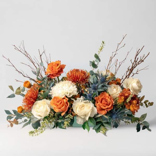 Low floral arrangement with orange and white roses and spiky blooms