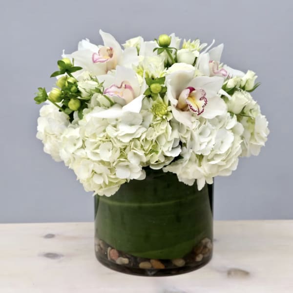 White hydrangeas and orchids arranged in a glass vase