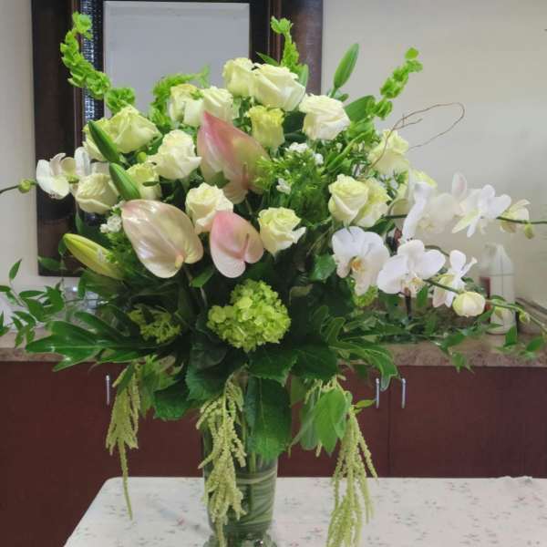 Large white and pale pink floral arrangement in a green glass vase